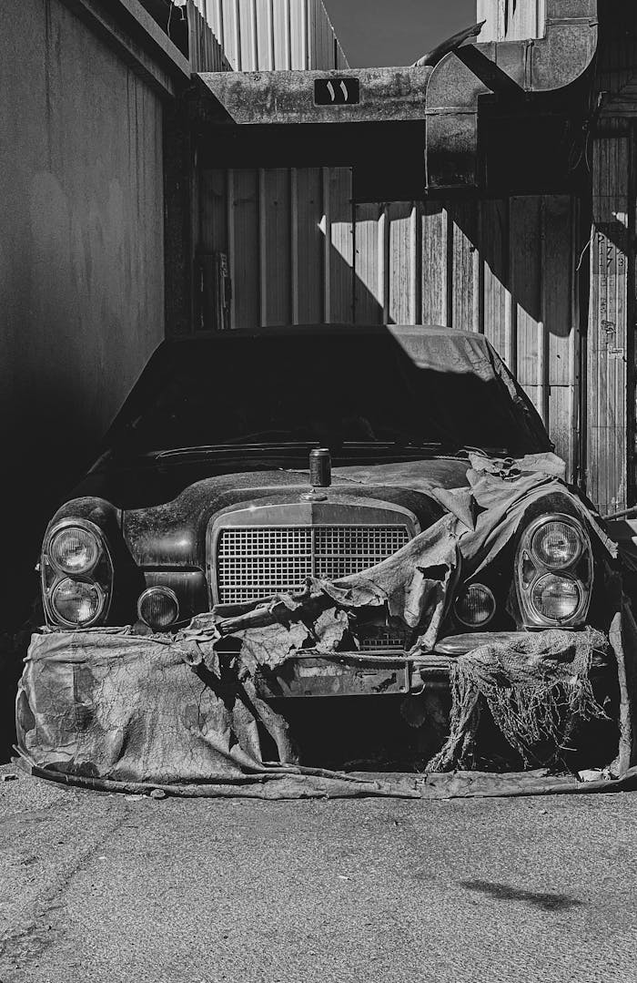 services-03 A black and white photo of a vintage abandoned car in an industrial setting.